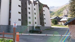 Un edificio a più piani con un ingresso chiuso da cancello, un'auto parcheggiata davanti e montagne sullo sfondo.