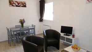 Un soggiorno con un tavolo da pranzo, due sedie, una TV e un piccolo tavolo con della frutta.