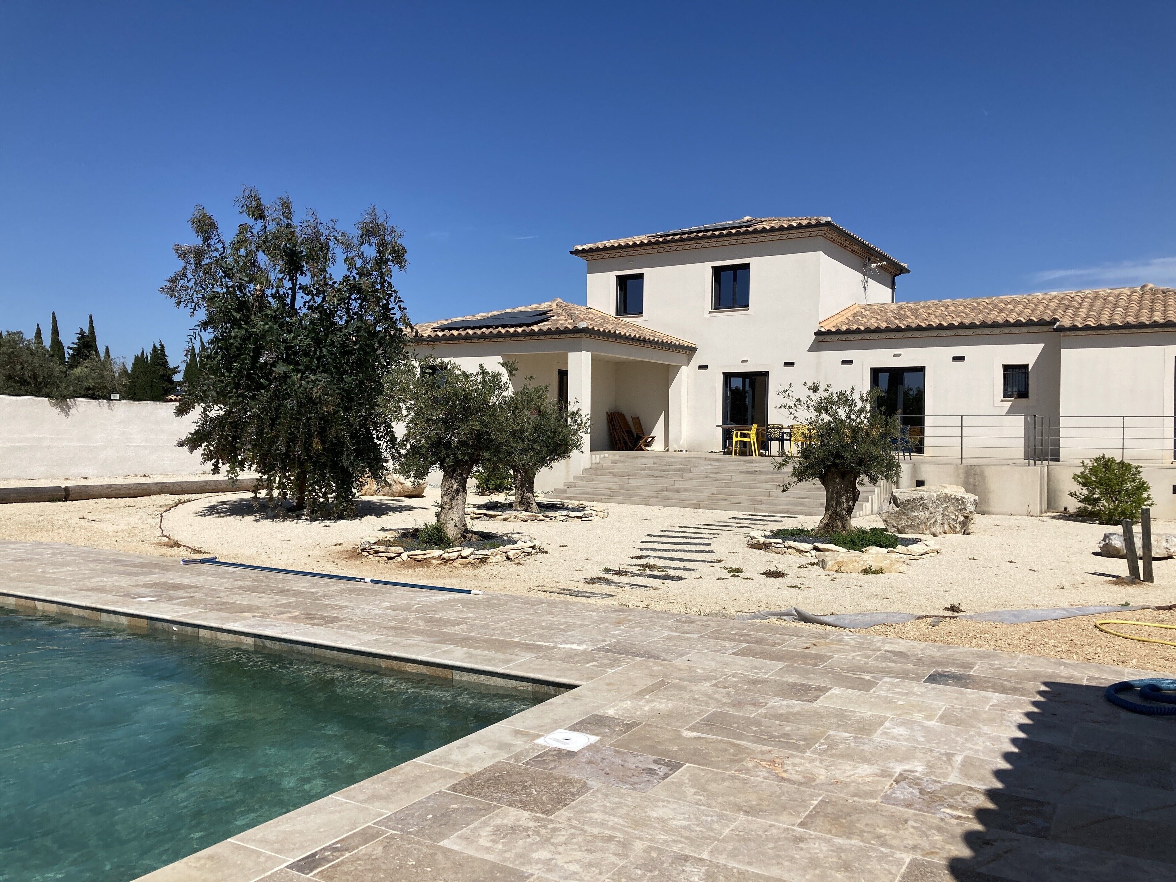 A two-story house with a swimming pool, outdoor seating, and a stone pathway leading to the entrance.