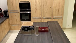 Moderni keittiö, jossa on puiset kaapit, keskellä sijaitseva saareke, jossa on liesi, sekä integroidut kodinkoneet.