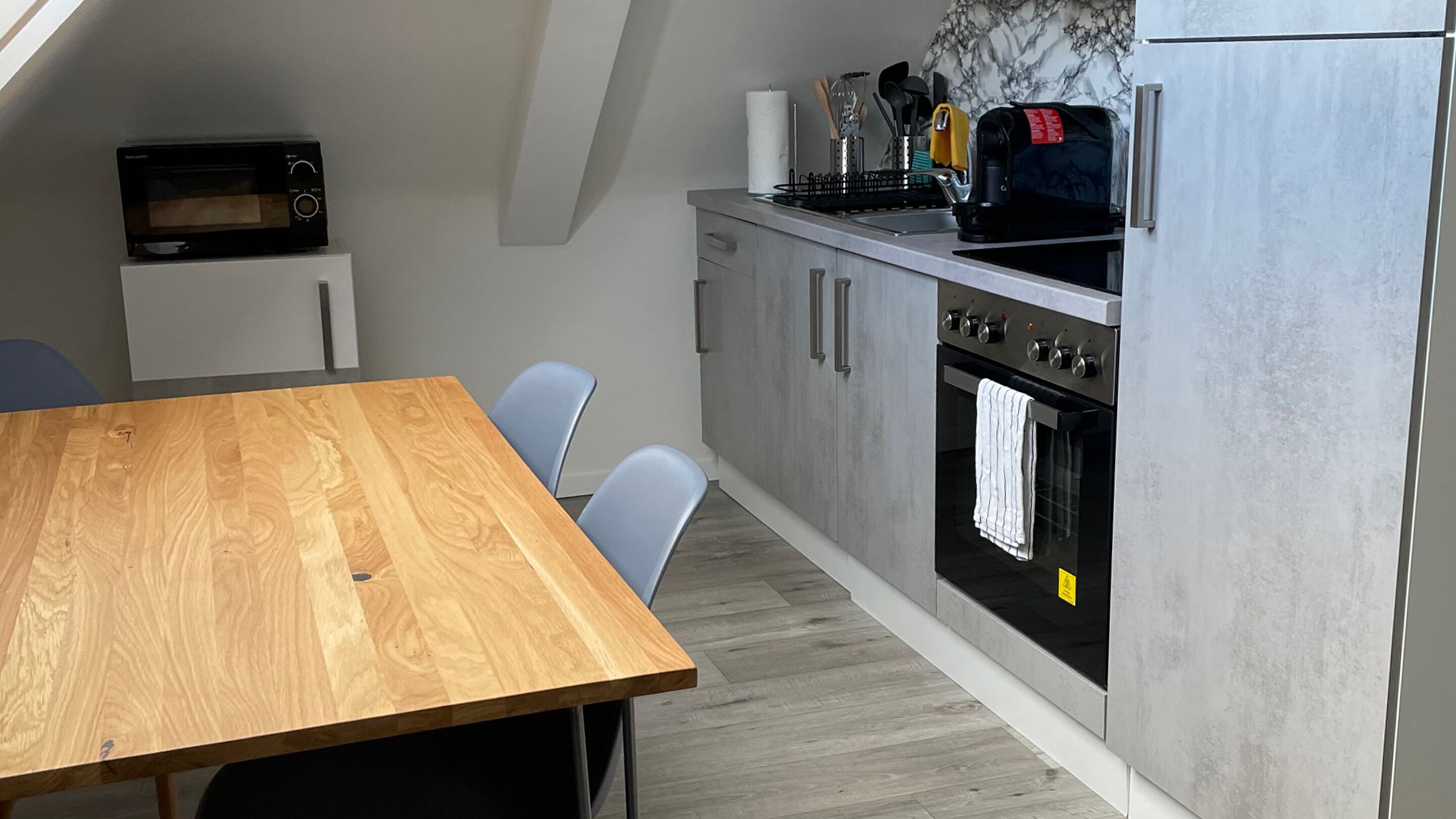 Una cocina compacta con una mesa de madera, horno empotrado, microondas y tostadora.