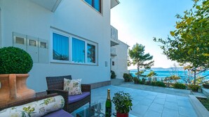 A modern outdoor seating area with a glass table, cushions, and a bottle of champagne. - Apartment Papilio (Brela)
