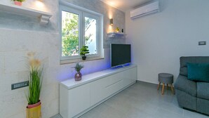 A modern living room with a TV on a white cabinet, a grey sofa, and a small stool. - Apartment Papilio (Brela)