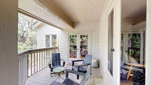 A covered porch with wooden railings, two Adirondack chairs, and a small round table. - Bright and cheery villa! Close to everything that resort has to offer! (Hilton Head Island)