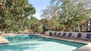 A rectangular pool with clear blue water, surrounded by lounge chairs and trees. - Bright and cheery villa! Close to everything that resort has to offer! (Hilton Head Island)