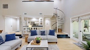 A modern living room with a grey sofa set, a coffee table with decorative items, and a spiral staircase leading to an upper level. - Bright and cheery villa! Close to everything that resort has to offer! (Hilton Head Island)