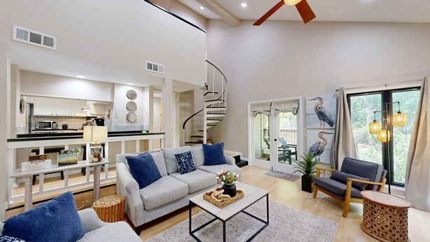 A modern living room with a grey sofa, a coffee table, and a staircase leading to a balcony. - Bright and cheery villa! Close to everything that resort has to offer! (Hilton Head Island)