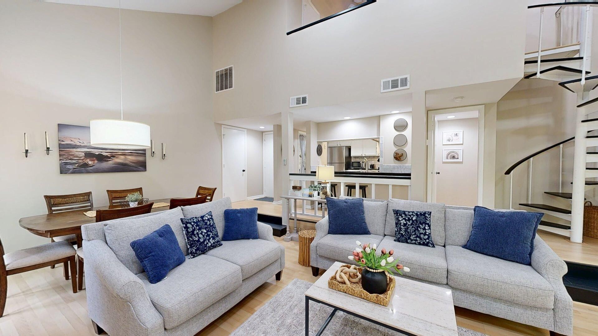 A spacious living area with two grey sofas, a dining table, and a kitchen in the background.