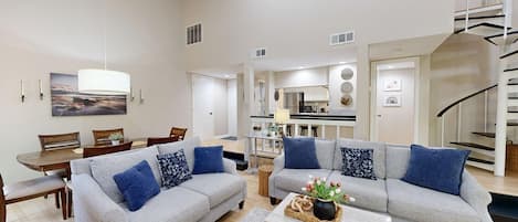 A spacious living area with two grey sofas, a dining table, and a kitchen in the background.