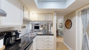 A modern kitchen with white cabinets, a black countertop, and a large wall clock. - Bright and cheery villa! Close to everything that resort has to offer! (Hilton Head Island)