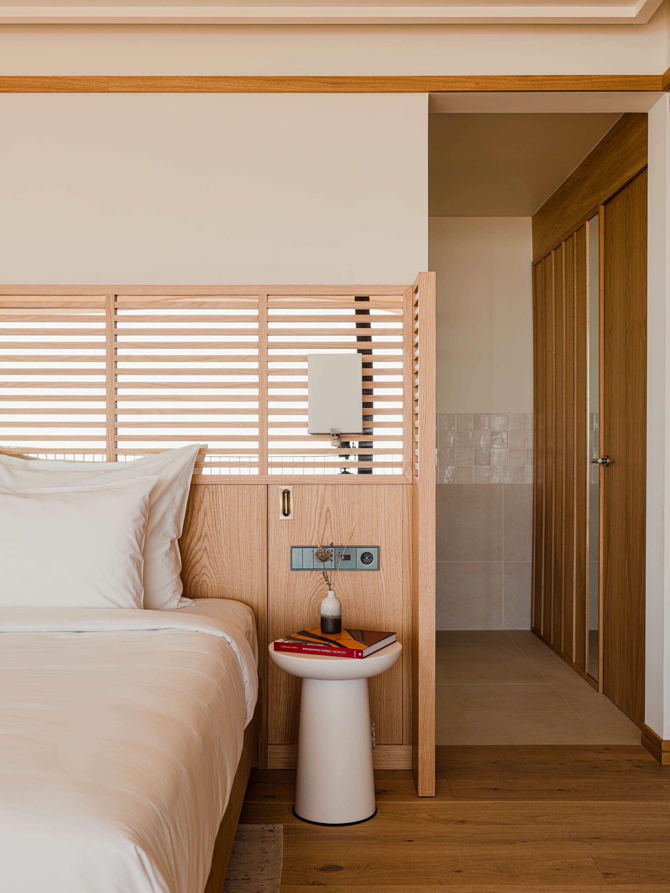 Une chambre à coucher avec un lit, une table de chevet sur laquelle se trouve un livre, un radiateur fixé au mur et une porte en bois.
