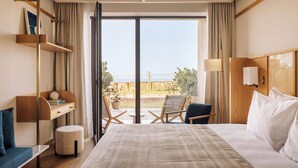 Habitación de hotel con cama, escritorio con silla, una mesita y vistas al exterior.