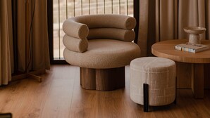 Una habitación moderna con un sofá curvo, una mesa redonda de madera y vistas a la playa a través de un amplio ventanal.