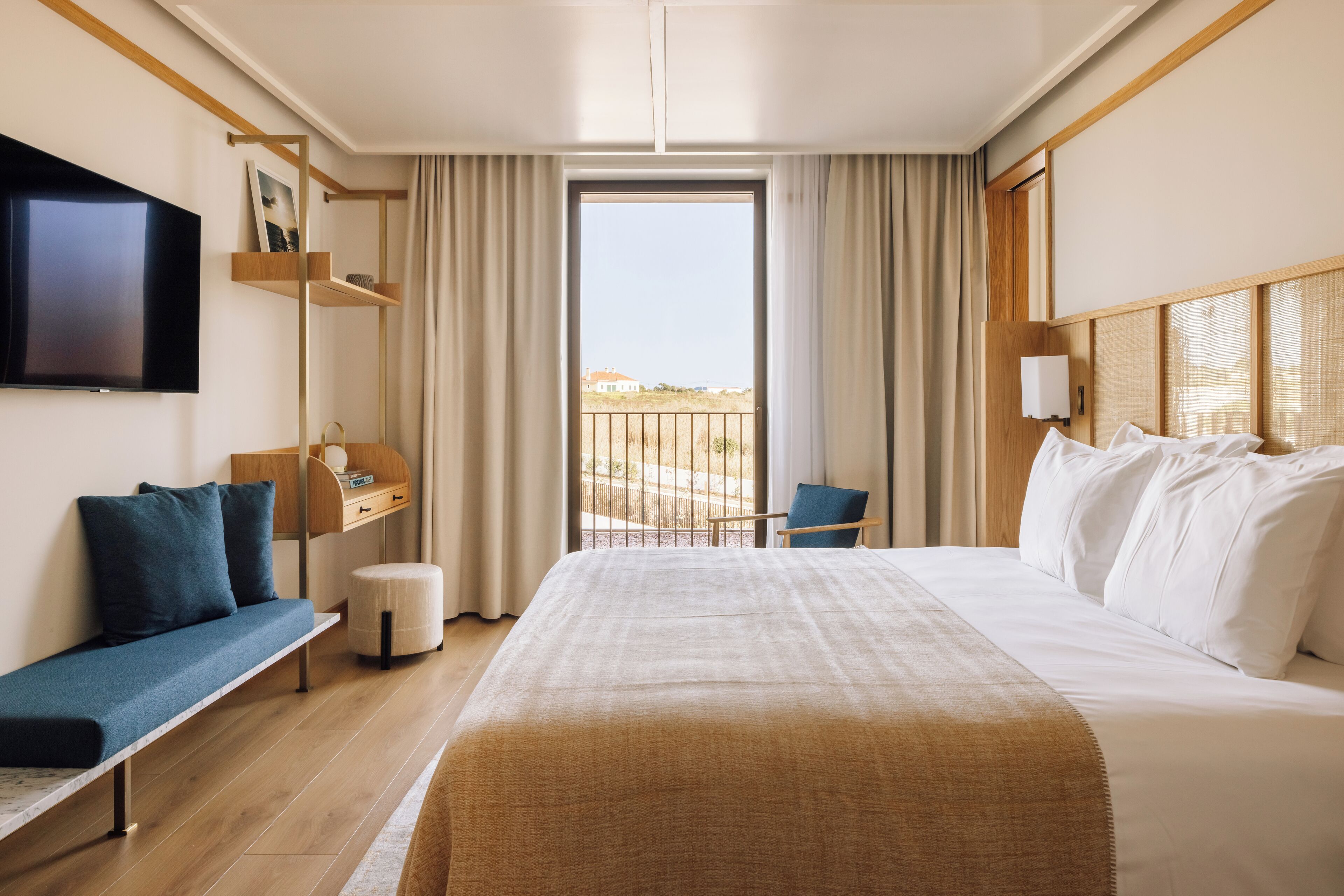Habitación de hotel con una cama grande, televisión montada en la pared, balcón con vistas y un escritorio con silla.
