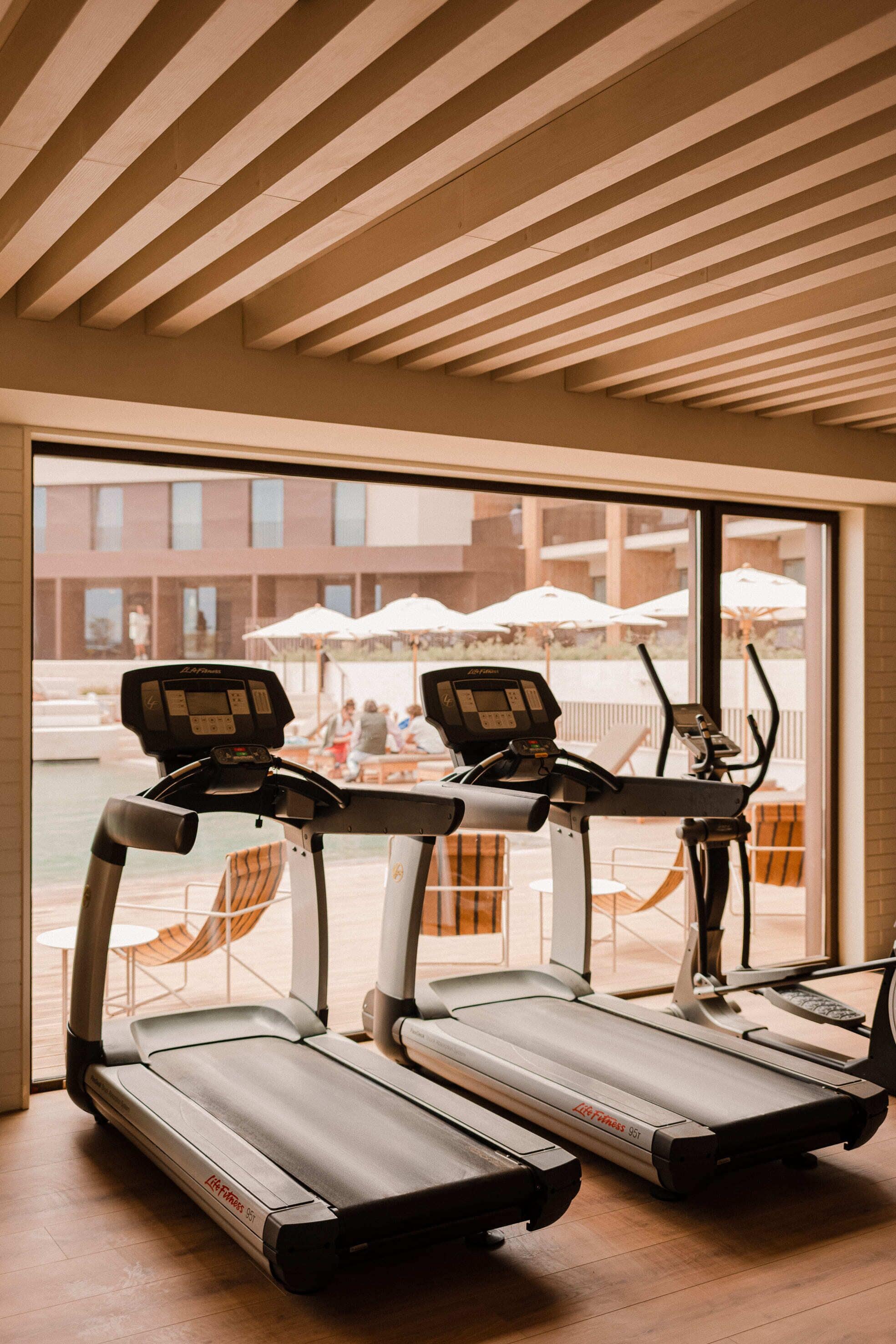 A gym with treadmills and a view of an outdoor seating area with umbrellas.