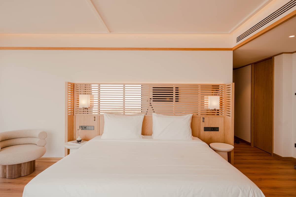 Ein modernes Schlafzimmer mit einem großen Bett, einem Holzkopfstück, Nachttischen und einem Sessel.