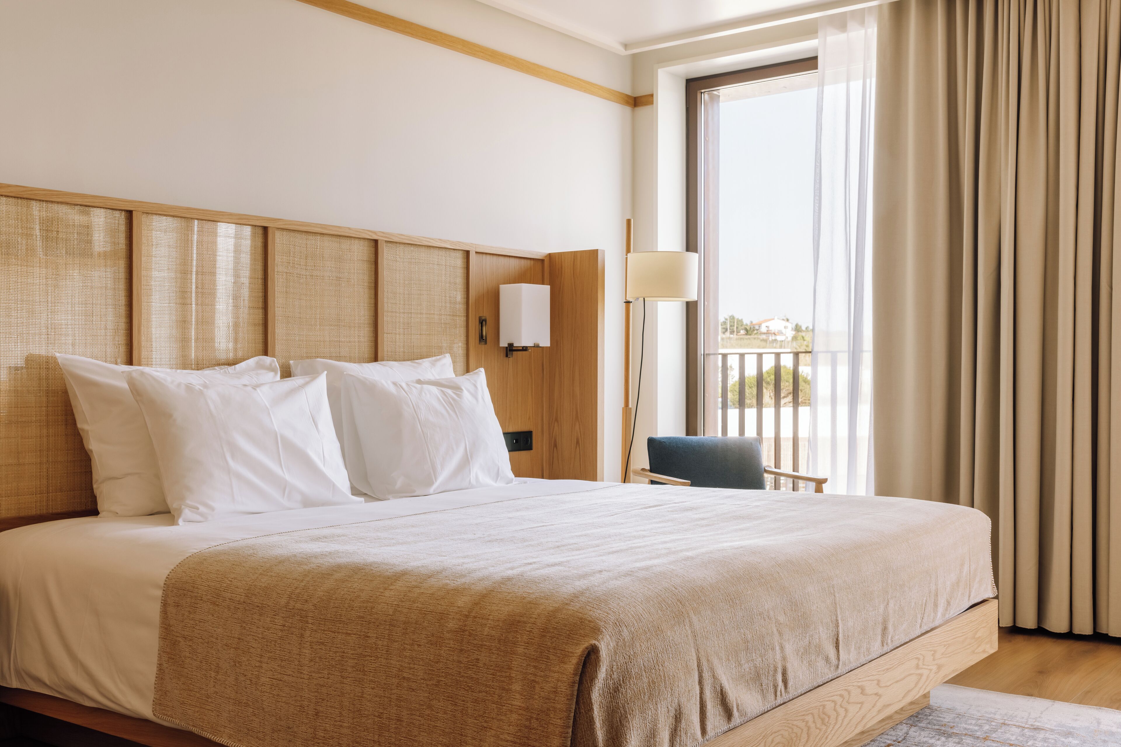 Ein Hotelzimmer mit einem großen Bett, einem hölzernen Kopfteil, einer Nachttischlampe und Blick ins Freie durch eine Schiebetür.