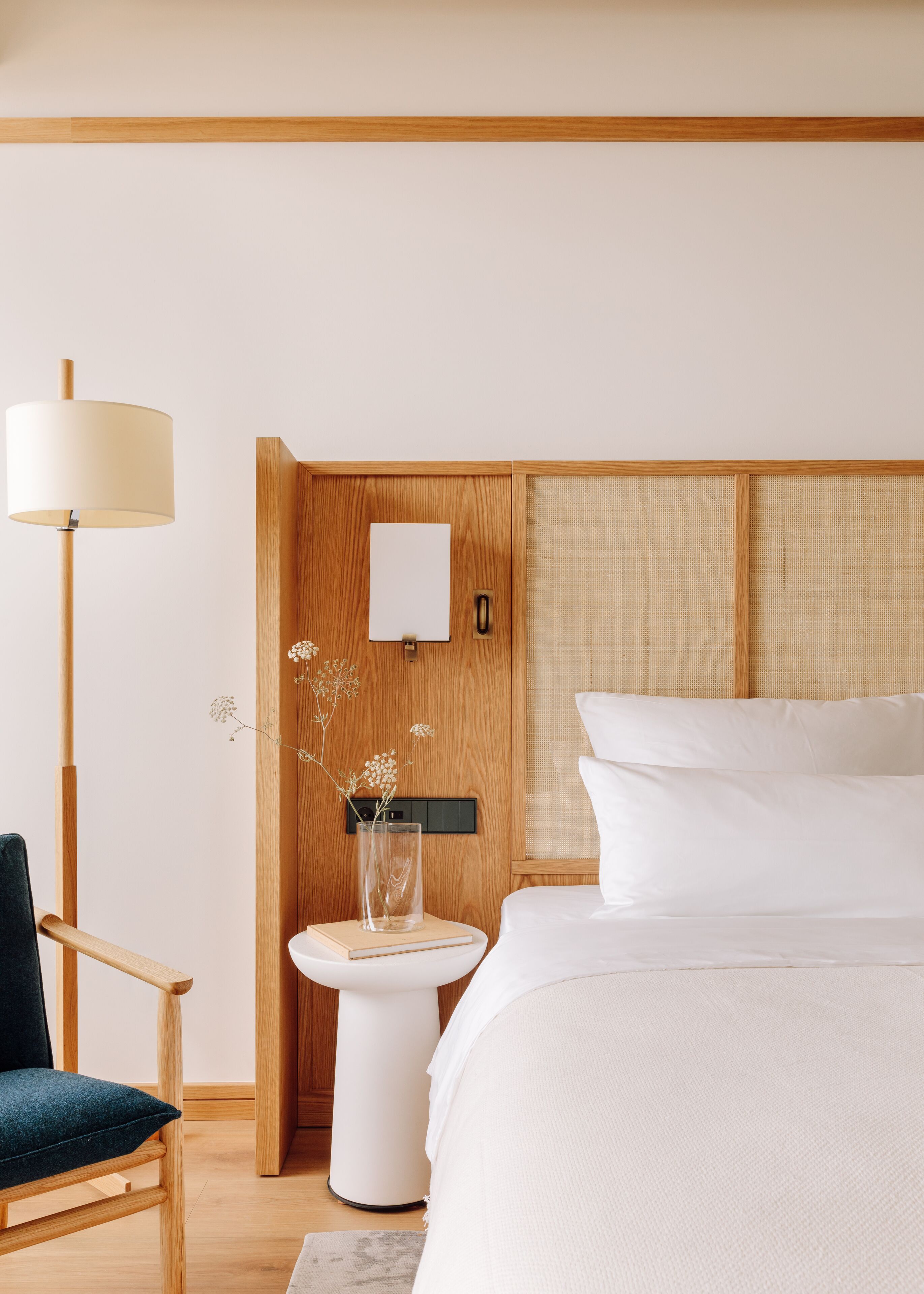 A bedroom with a bed, bedside table, lamp, chair, and a wooden wardrobe.