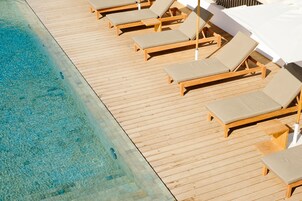 Una terraza de madera con sillones de descanso y una piscina.