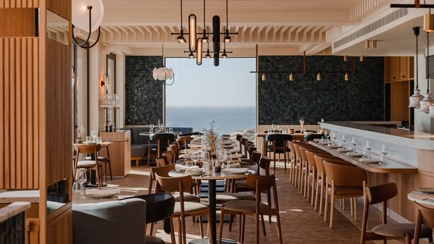 Un restaurante con un amplio comedor, sillas de madera y vistas al océano.