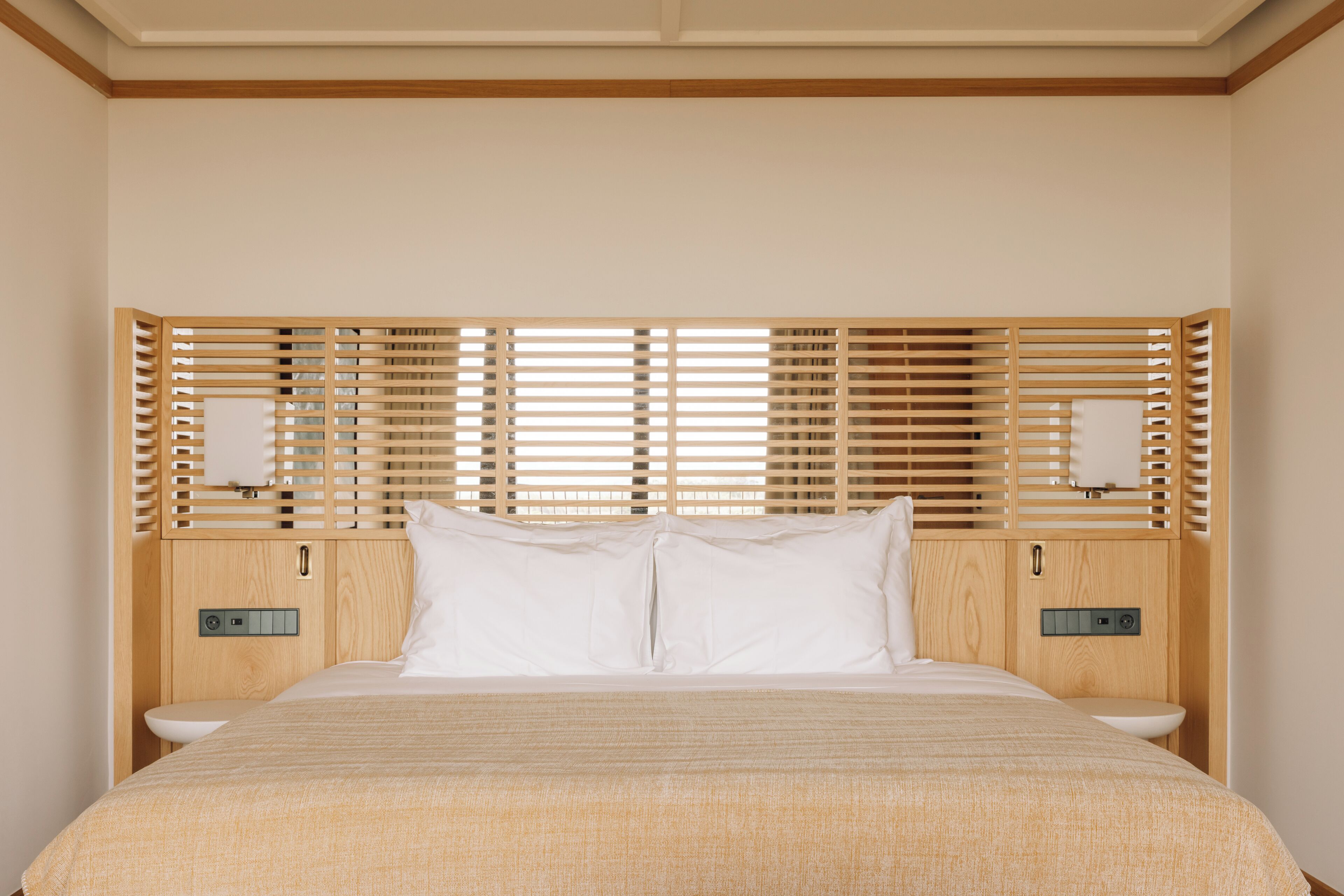 Un dormitorio moderno con cabecera de madera, una cama grande, dos mesitas de noche y una estantería empotrada.