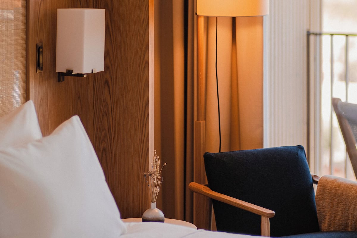 Ein Hotelzimmer mit Bett, Nachttisch, Lampe, Stuhl und Blick ins Freie.