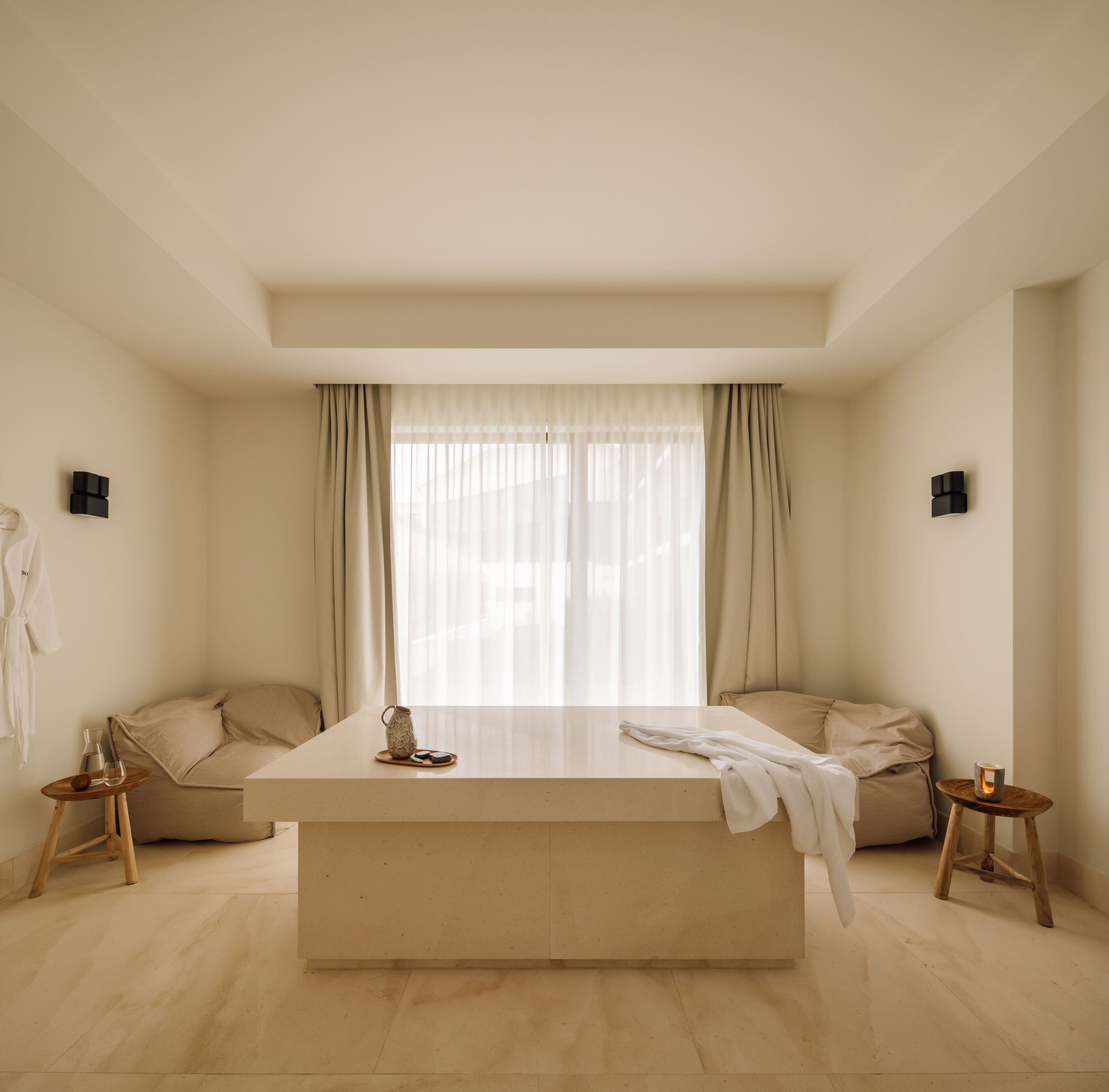 A modern bedroom with a large bed, two bedside tables, a window with sheer curtains, and a light-colored floor.
