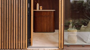 Entrada de un spa con fachada de madera, un cartel que indica la zona de spa y un mostrador de recepción con un florero y una vela.