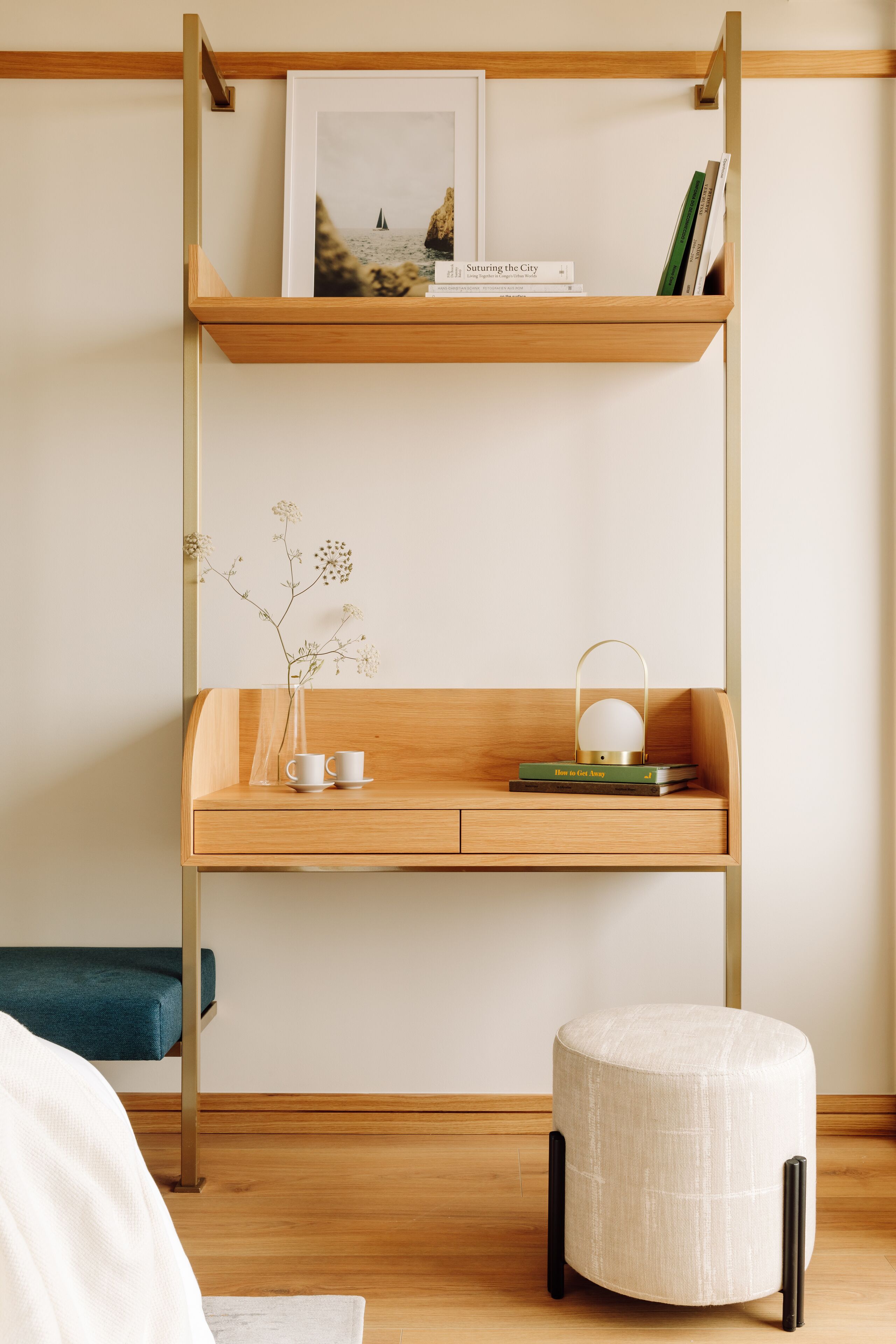 A modern room with a wooden desk, a hanging shelf, and a small round ottoman.