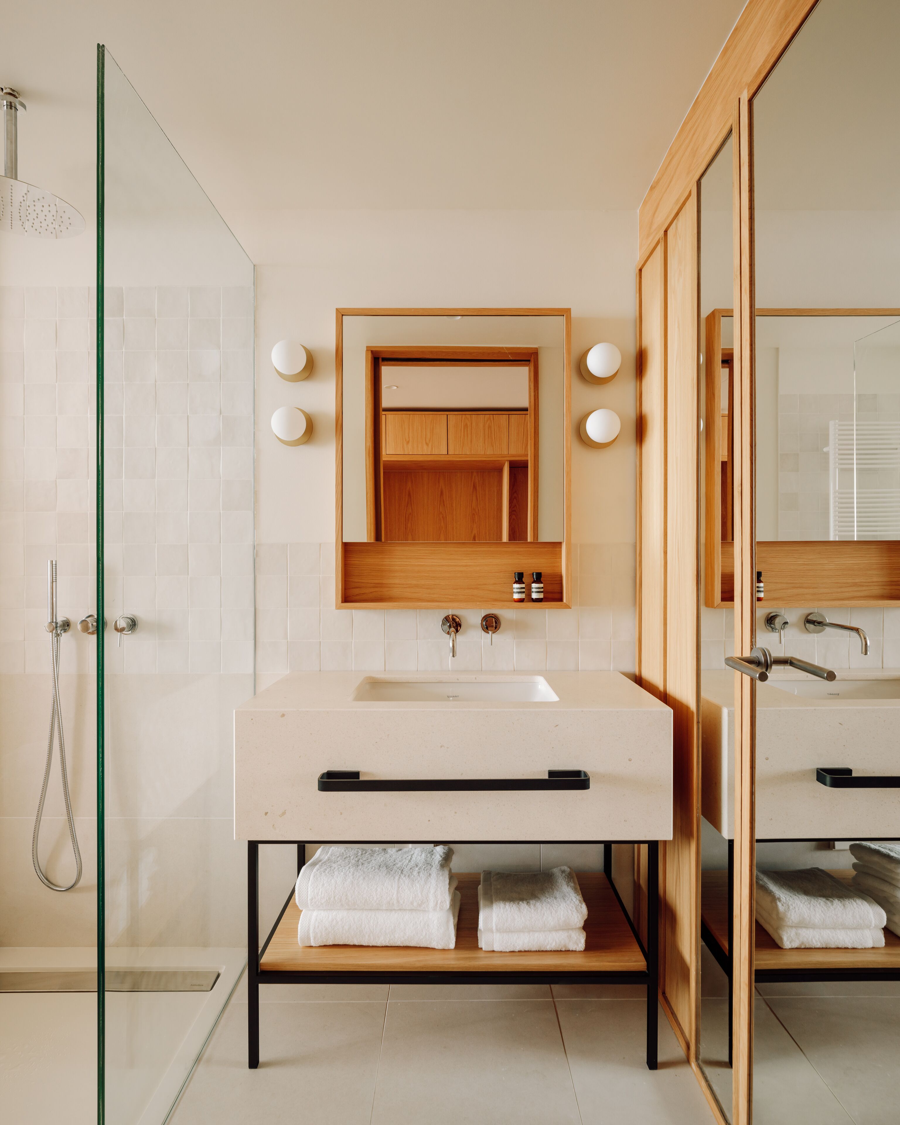 Un baño moderno con cabina de ducha de vidrio, tocador de madera con lavabo y espejo sobre el tocador.