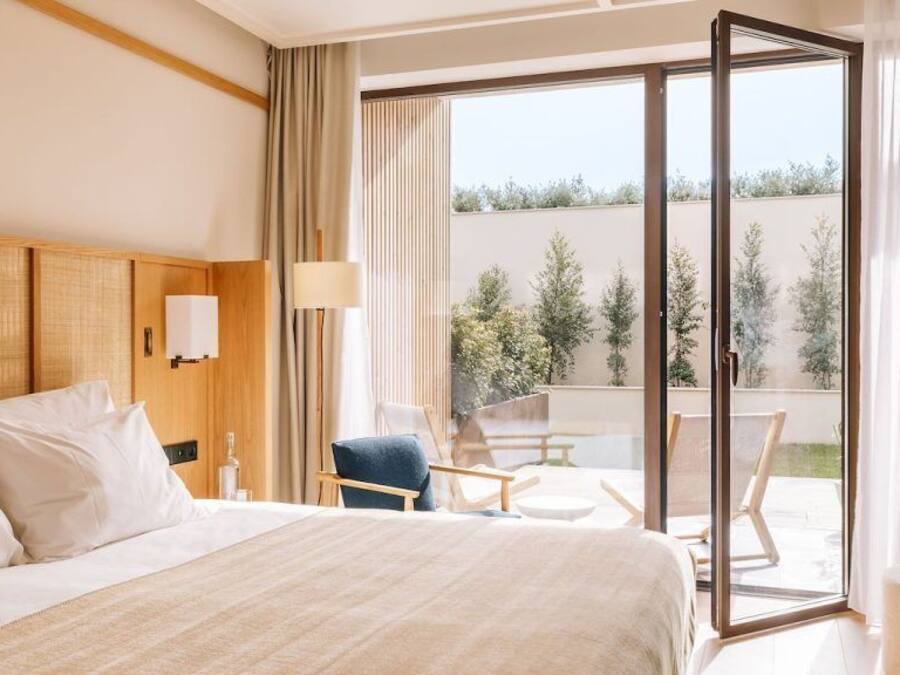 Een hotelkamer met een groot bed, een stoel, een tafel en een schuifdeur naar een buitenruimte.