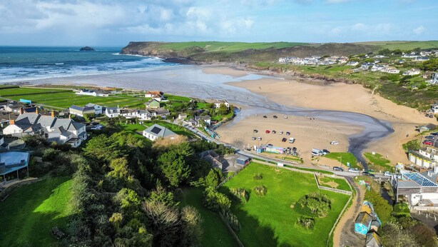 Uma cidade costeira com uma praia arenosa, campos verdes e casas.