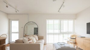 Uma sala de estar minimalista com um sofá, um banquinho e uma TV sobre um móvel de madeira.