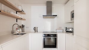 Uma cozinha moderna com armários brancos, eletrodomésticos de aço inoxidável e prateleiras de madeira.