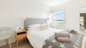 Quarto com cama, mesa de cabeceira, abajur e vista para o exterior.