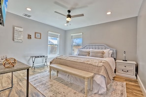 Une chambre à coucher comprenant un lit, une table de chevet, un banc, une commode, un ventilateur de plafond et des fenêtres.
