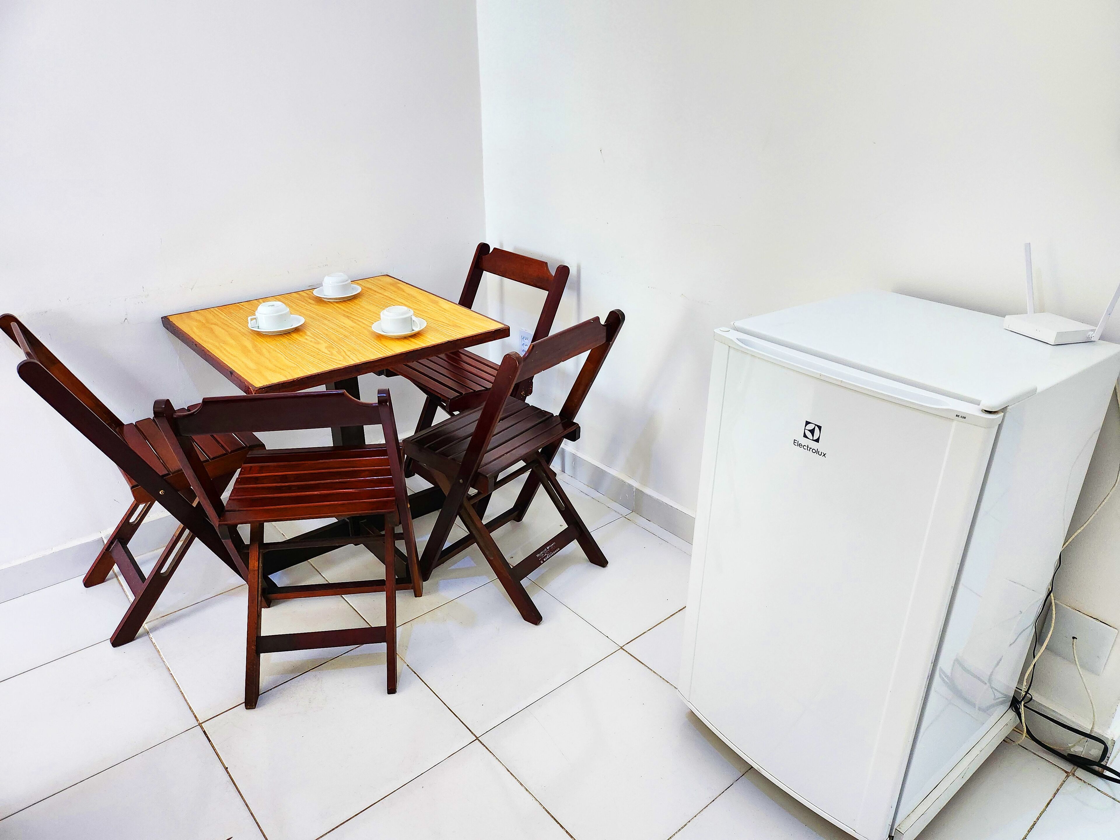 A small dining area with a wooden table and four chairs, a white refrigerator, and a tiled floor.