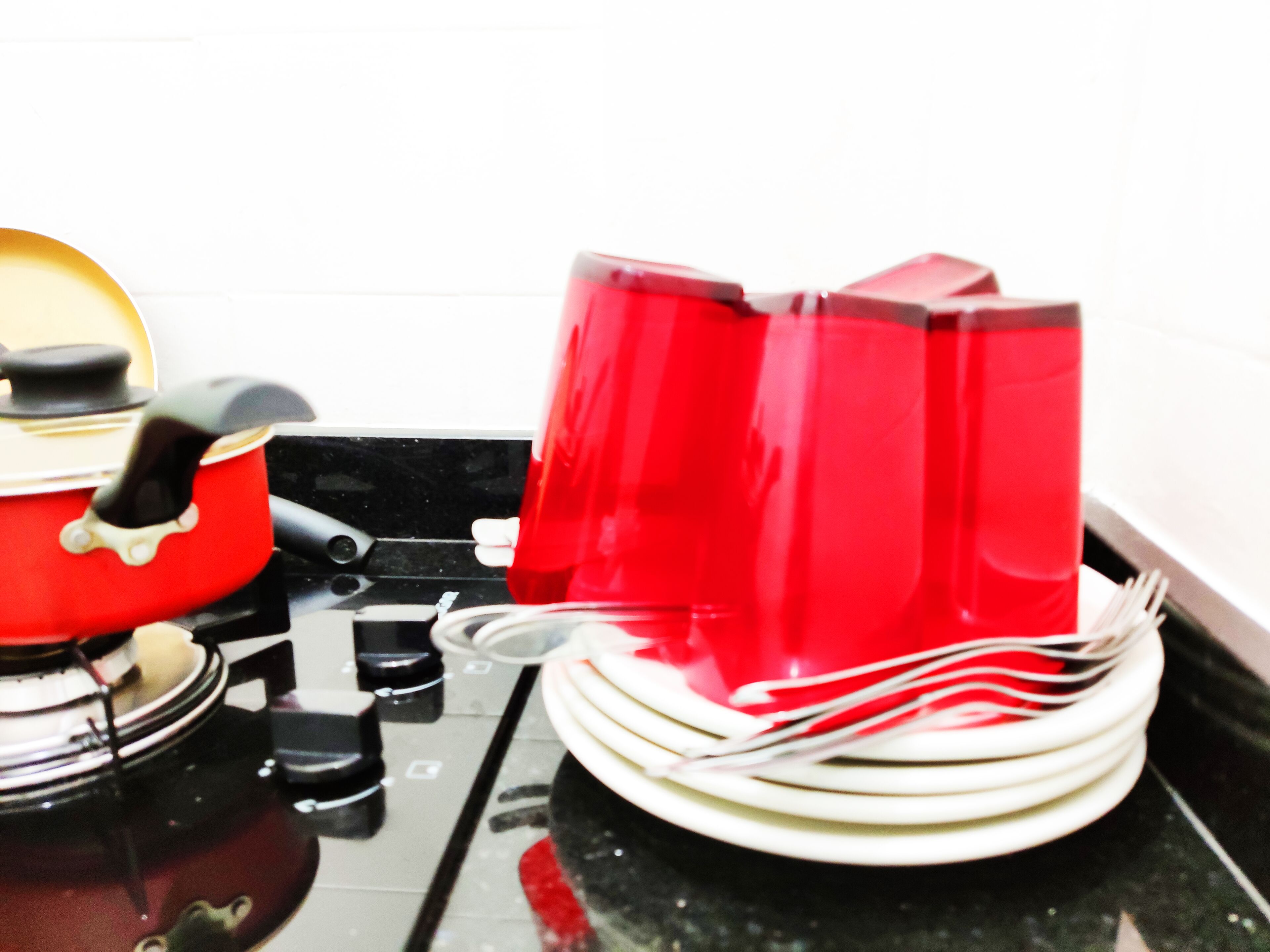 Una cucina con una pentola rossa sul fornello, un bollitore rosso e una pila di piatti bianchi.
