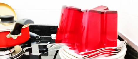 A kitchen with a red pot on the stove, a red kettle, and a stack of white plates.