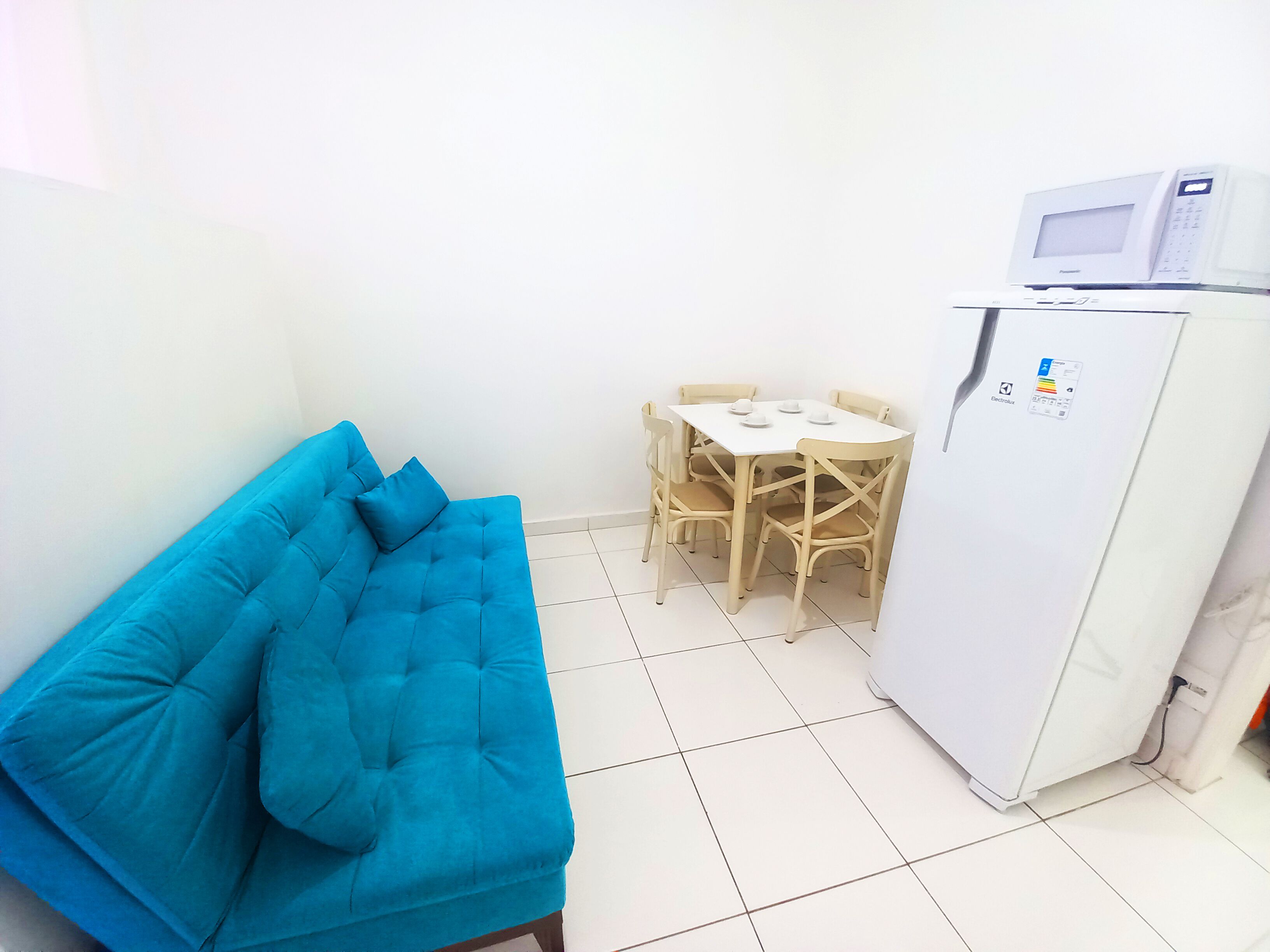 A small room with a blue sofa, a white table with four chairs, and a white refrigerator.