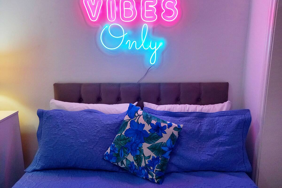 Una cama con un letrero de neón que dice 'GOOD VIBES Only'.