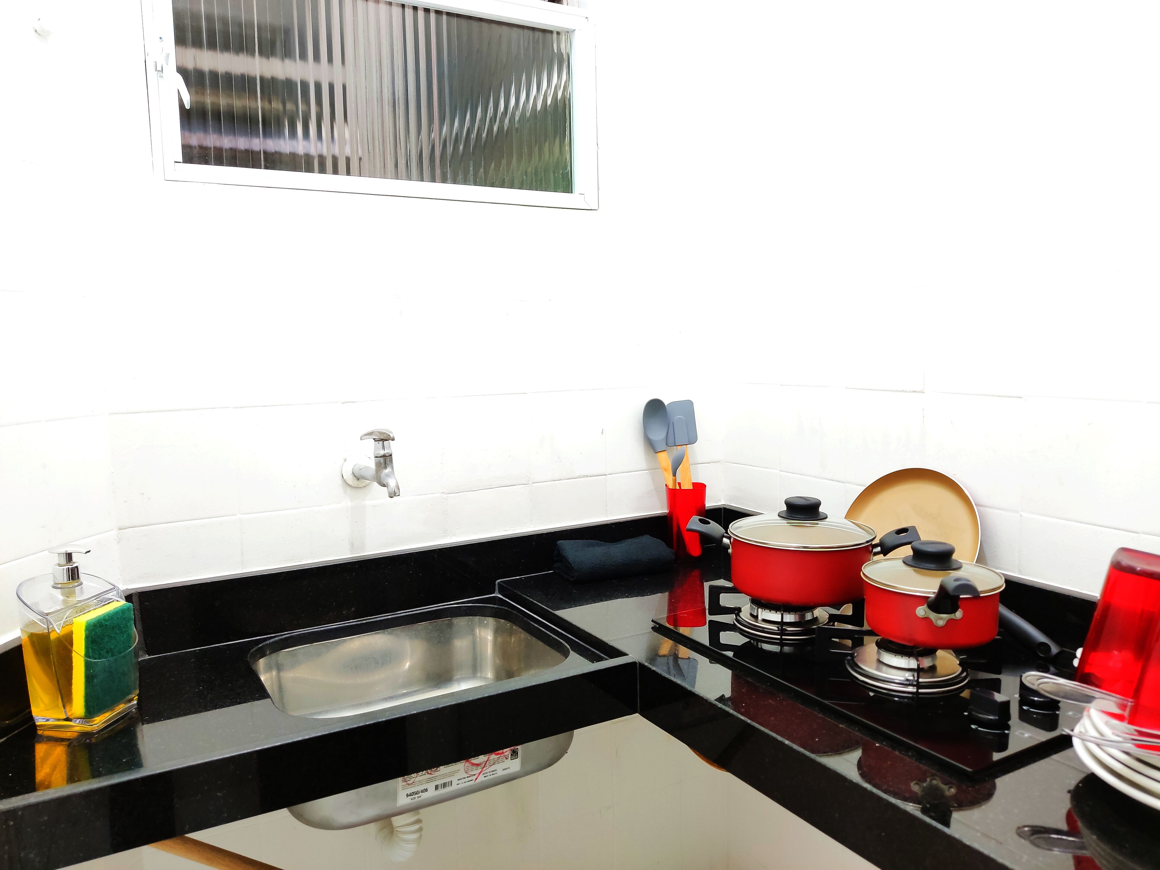Une cuisine dotée d’un plan de travail noir, d’un évier en acier inoxydable, d’une cuisinière à gaz rouge et d’une fenêtre avec des stores.