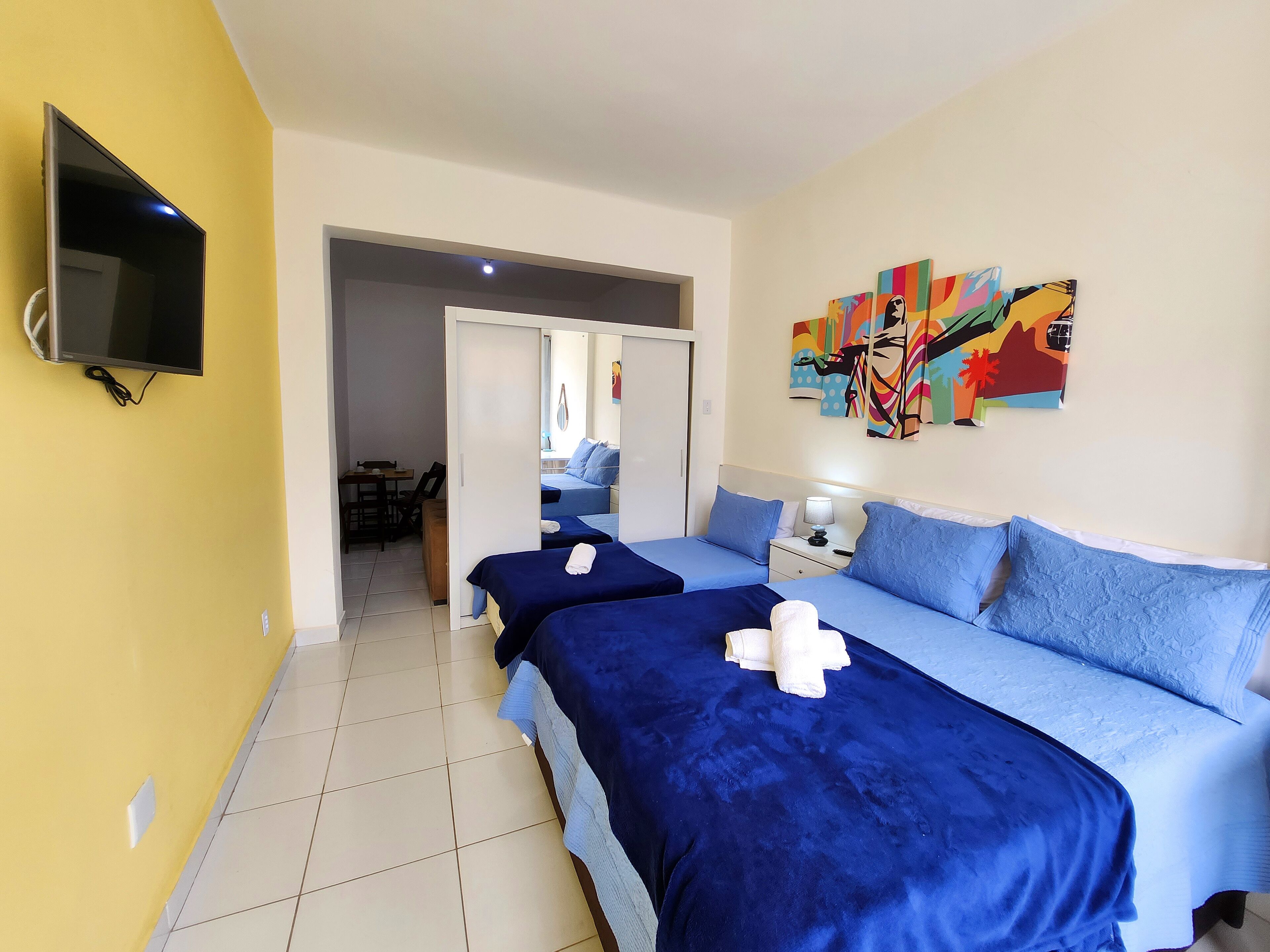 Habitación de hotel con dos camas, un televisor y arte colorido en la pared.
