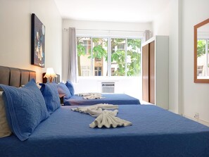 A hotel room with two beds, a large window with a view of greenery, a ceiling fan, and a wall-mounted air conditioner. - Copacabana Best Spot (Rio de Janeiro)