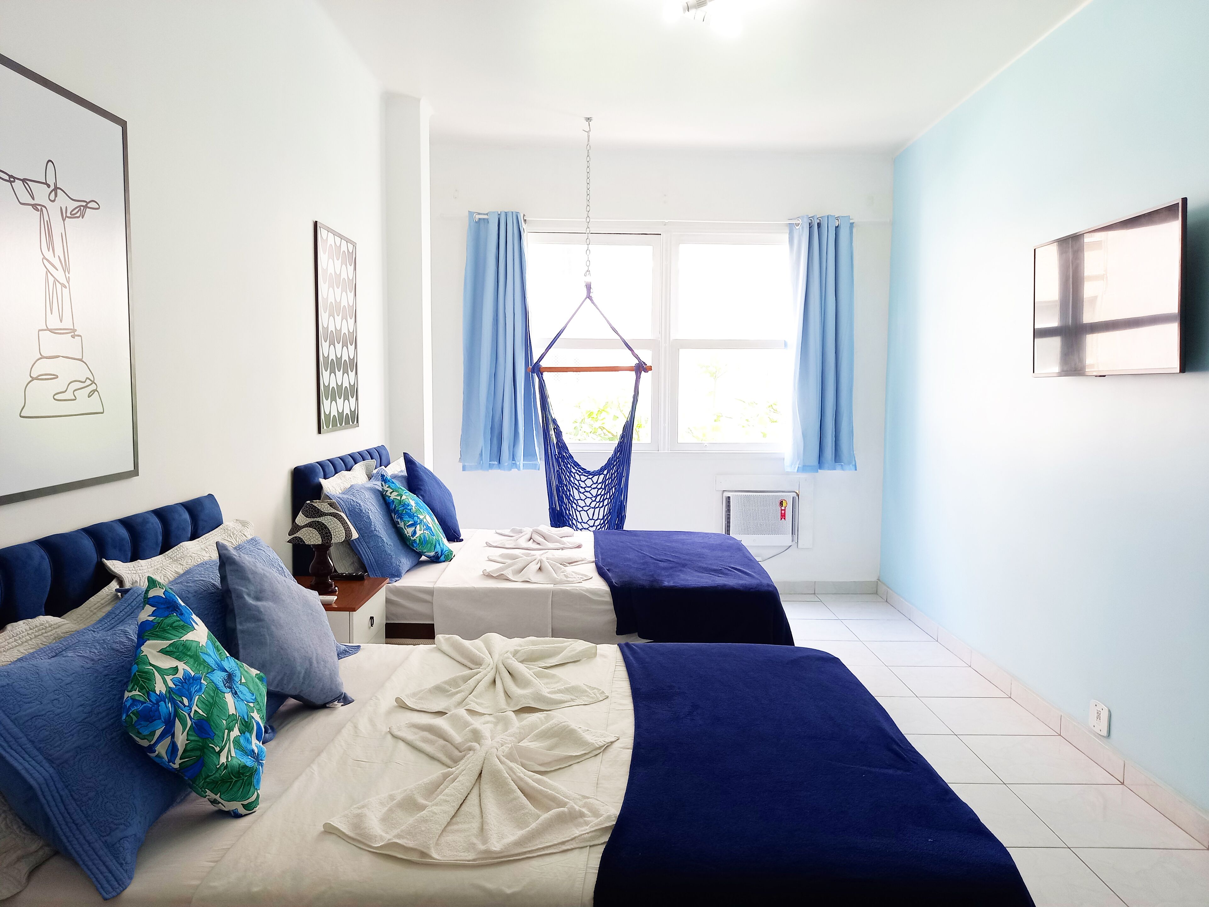 A bedroom with two beds, a hammock, and a large window with curtains.