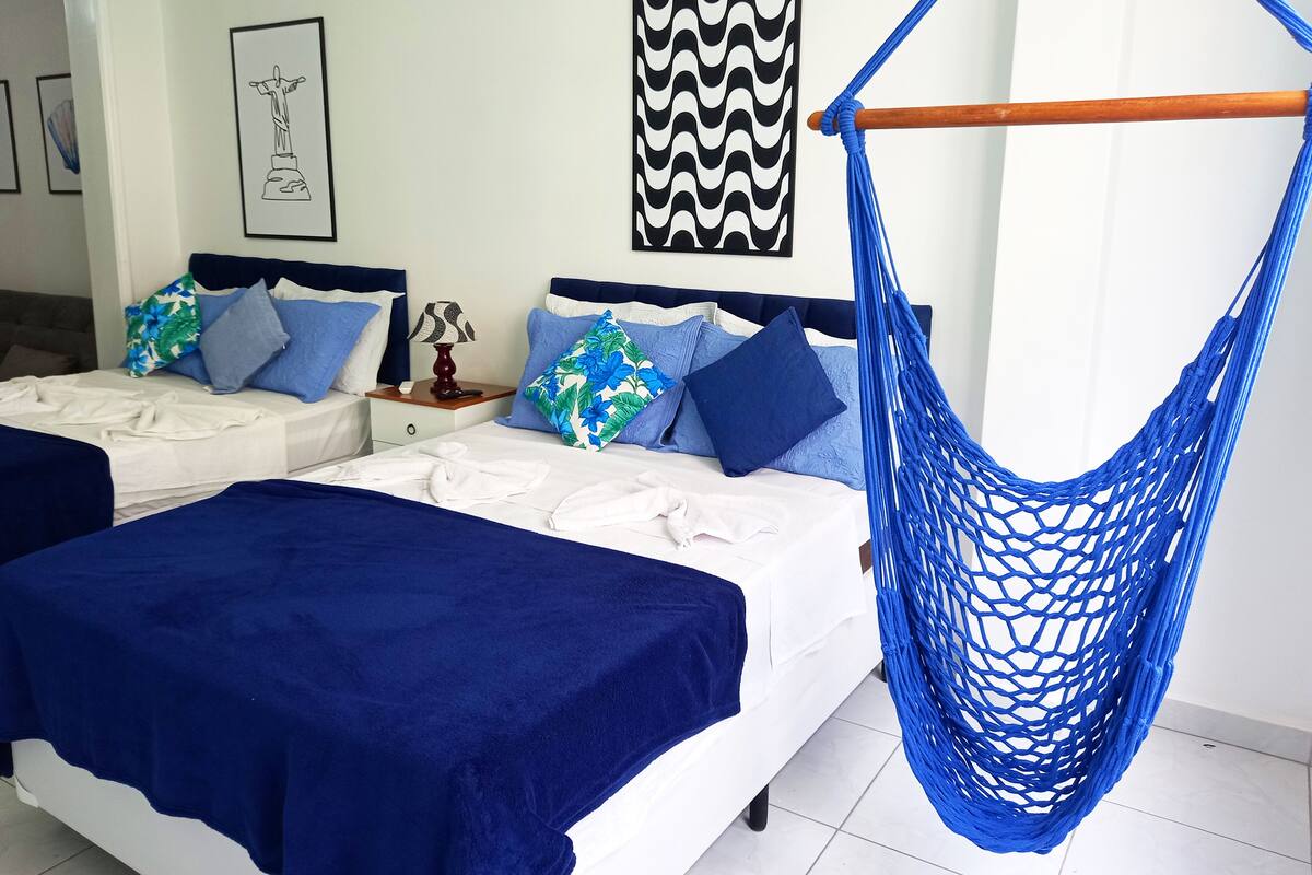 Habitación de hotel con dos camas, una hamaca y una mesita de noche con lámpara.