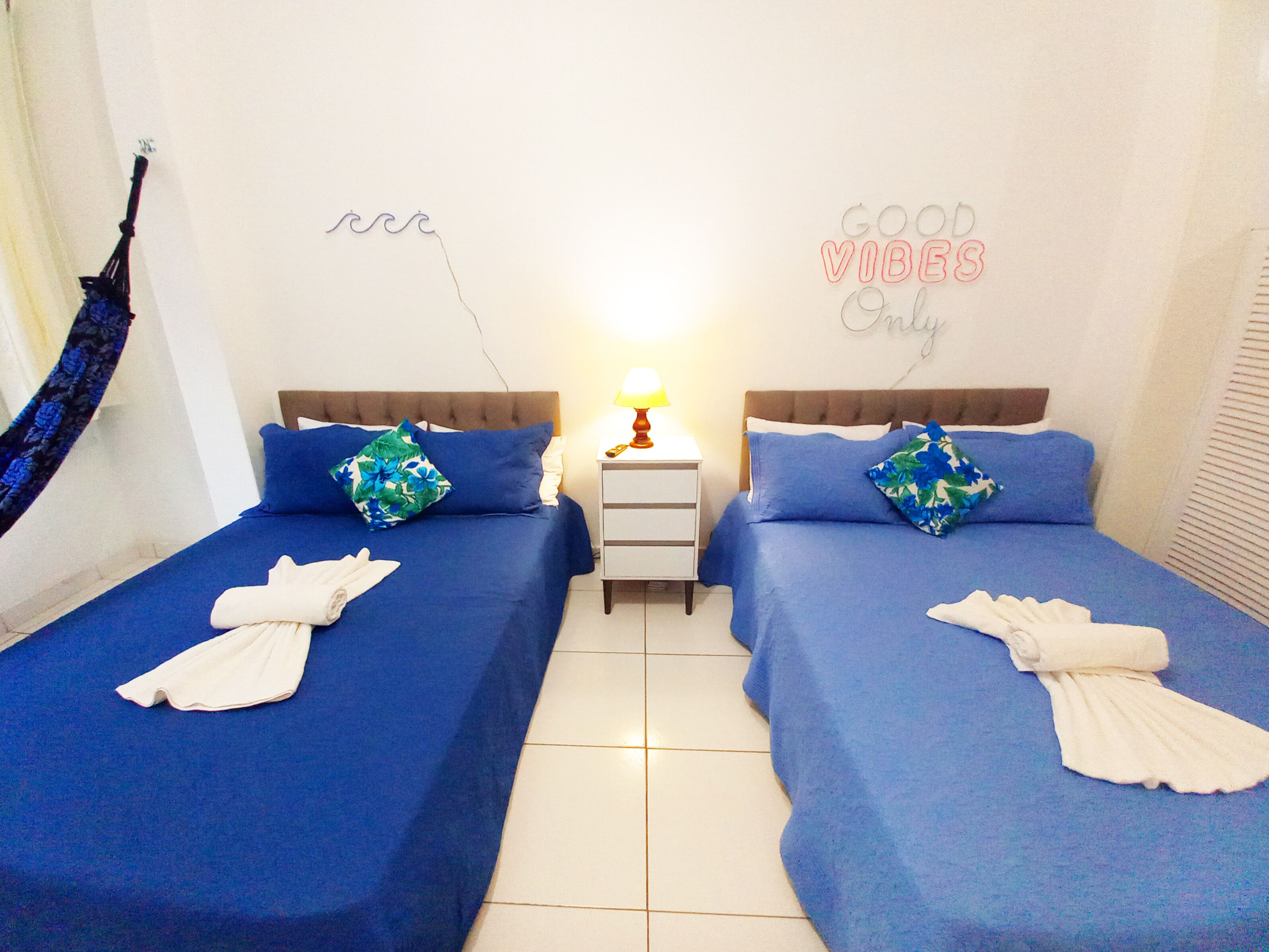 A twin room with two beds, each with a blue bedspread and matching pillows. There is a nightstand with a lamp between the beds.