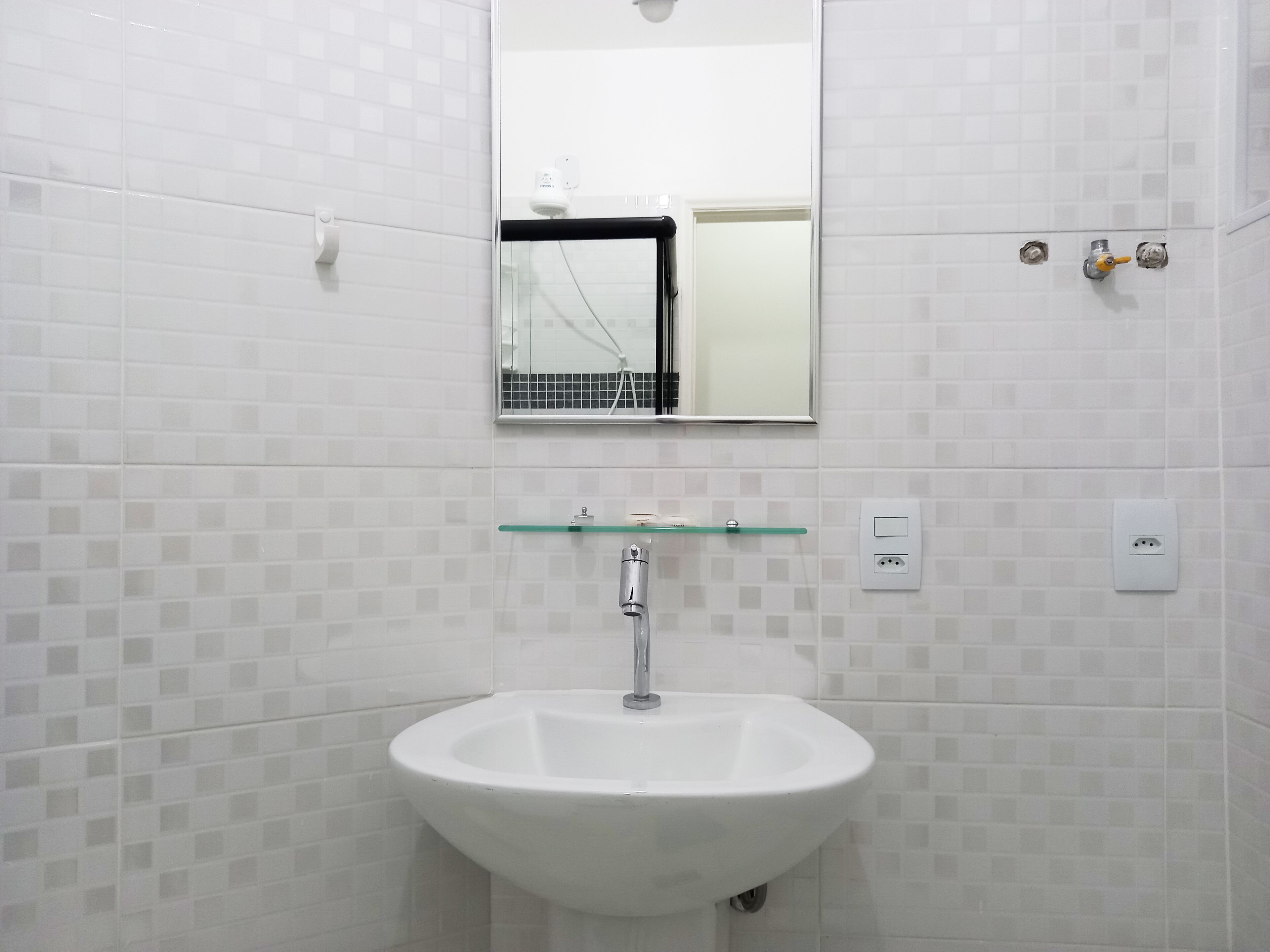 A bathroom with a white sink, a glass shelf above it, and a mirror.