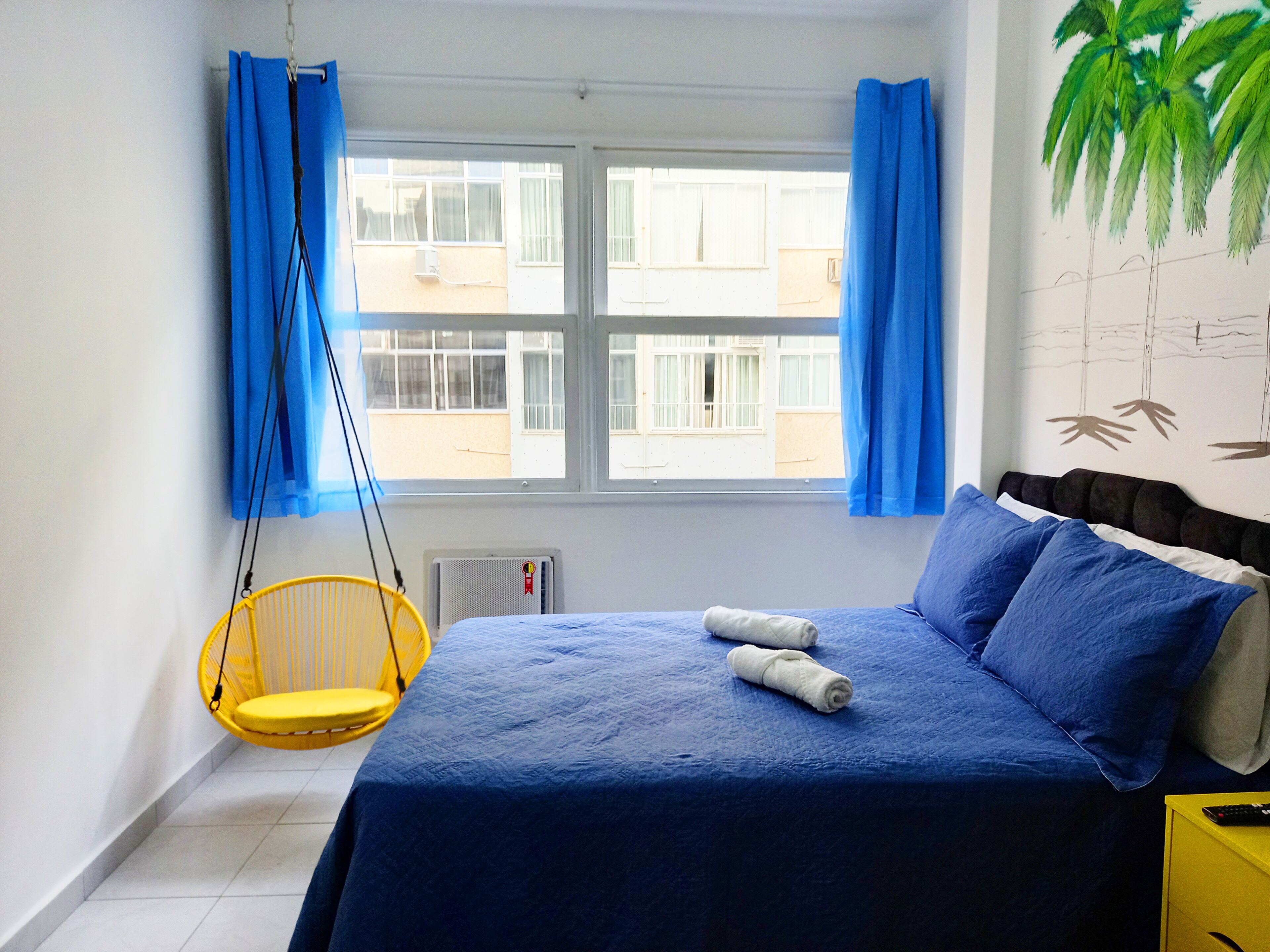 A bedroom with a bed, a hanging chair, and a window with curtains.