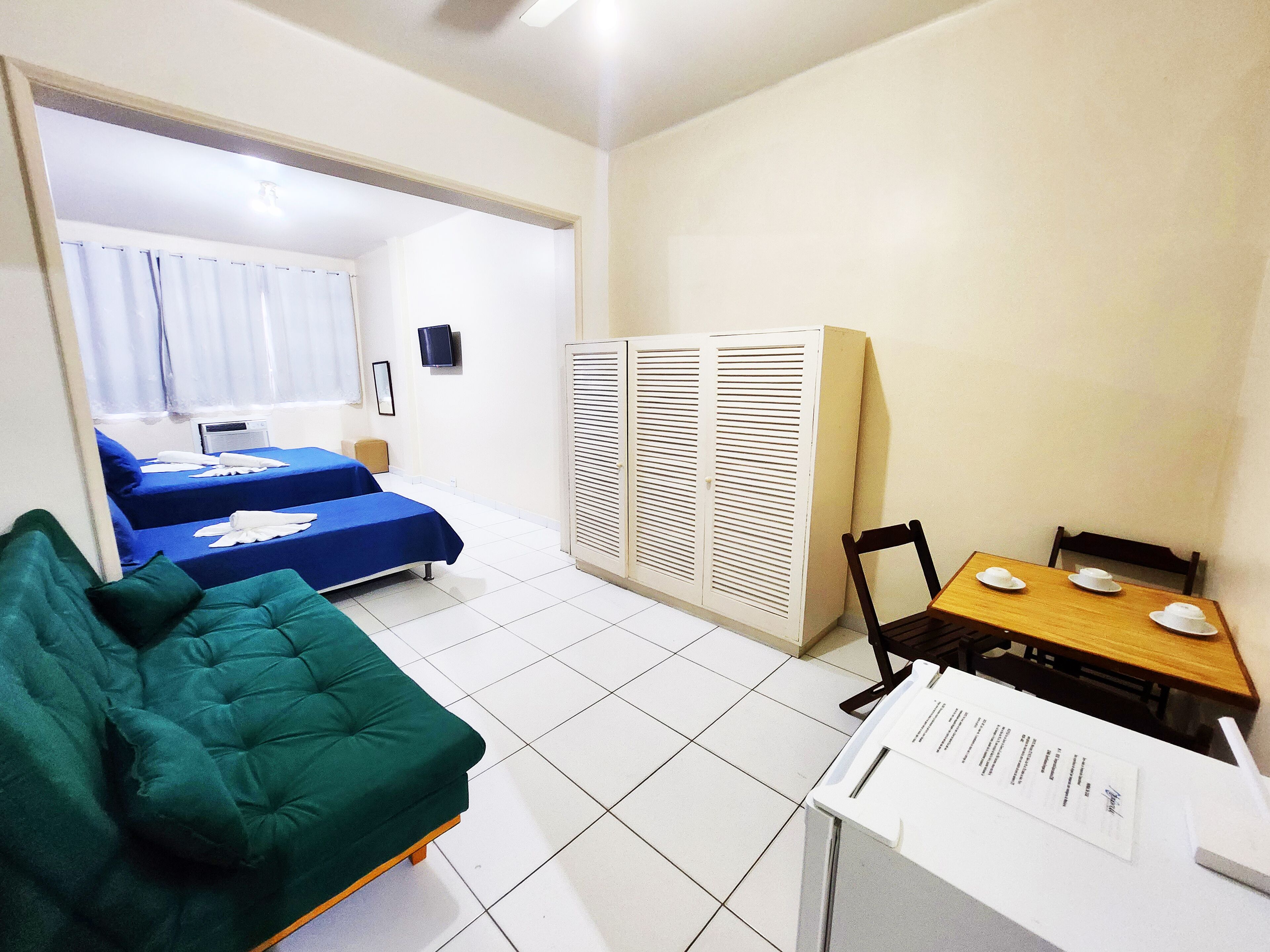 A hotel room with a bed, a green sofa, a small table with a chair, and a wardrobe.